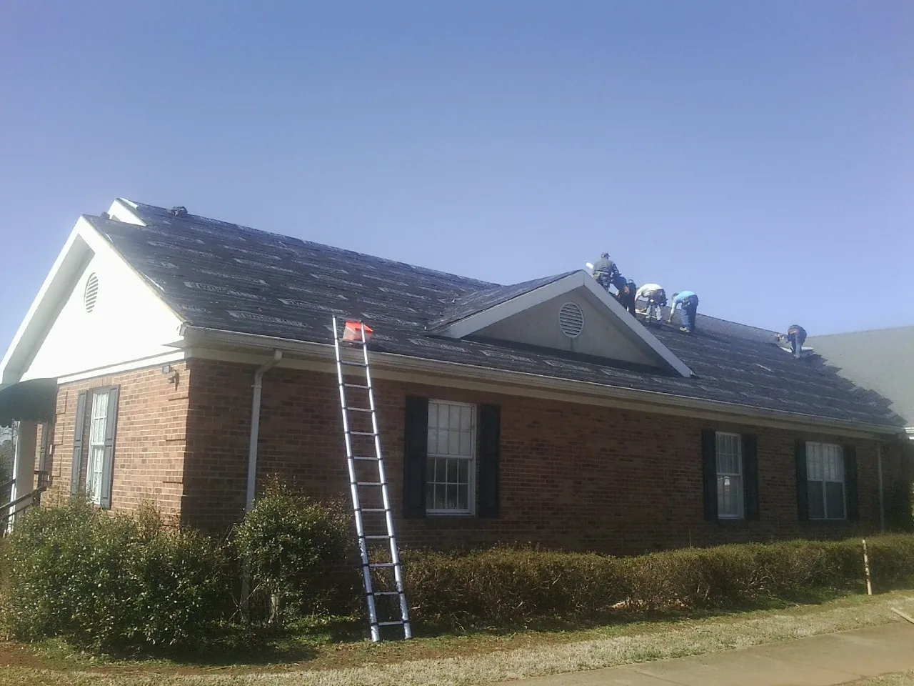Crew tearing shingles off a brick ranch roof with a ladder set — Emergency Roof Repair work by our crew in Marathon